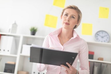 Genç sarışın bir kız ofiste üzerinde çıkartmalar ve ellerinde kalemle şeffaf bir panonun yanında duruyor..