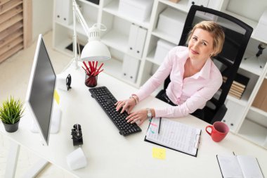 Genç bir kız ofiste bir masada oturan ve klavyede yazarak.