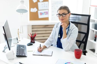 Beyaz bir elbise içinde genç bir kız ofiste masalarda oturur ve bir kalem elinde tutar. Bir stetoskop boynunda asılı.
