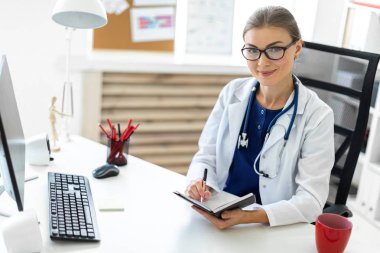 Beyaz bir elbise içinde genç bir kız ofiste bir masada oturur ve bir kalem ve defter elinde tutar. Bir stetoskop boynunda asılı.