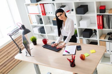 Genç bir kız masanın ayakta ve metin klavyede yazarak. Belgeler ve bir işaretleyici kızın yanında yalan.