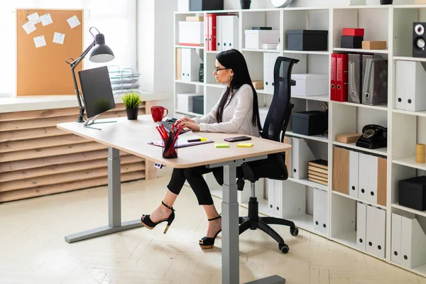 Uma jovem está sentada à mesa e digitando texto no teclado . — Fotografia de Stock