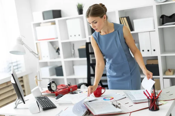 Een jong meisje staat in de buurt van een tafel in het kantoor en de rollen door de documenten. — Stockfoto