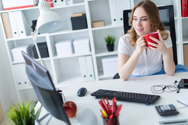 Mooi jong meisje werken met de computer in kantoor. Het meisje heeft een rode kop in haar handen. — Stockfoto