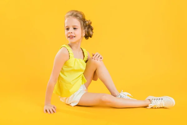 Ein Teenager-Mädchen sitzt auf gelbem Hintergrund. — Stockfoto