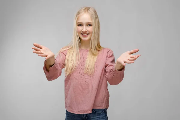 Ritratto di attraente sorridente dolce adorabile ragazza bionda adolescente in occhiali in camicetta rosa con le braccia aperte su sfondo grigio — Foto Stock