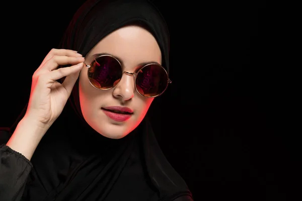 Portrait de belle jeune femme musulmane élégante portant du hijab noir et des lunettes de soleil comme concept de mode orientale moderne posant sur fond noir — Photo