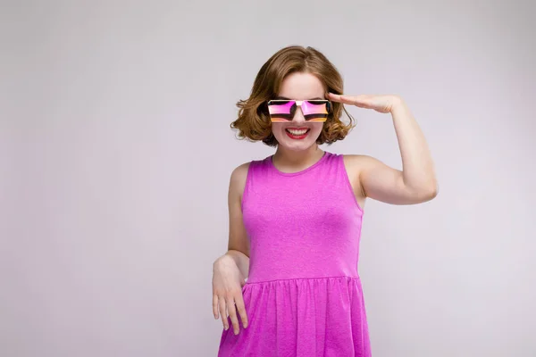 Charmante junge Mädchen in rosa Kleid auf grauem Hintergrund. fröhliches Mädchen mit quadratischen Gläsern. das Mädchen legte ihr die Hand an den Kopf — Stockfoto
