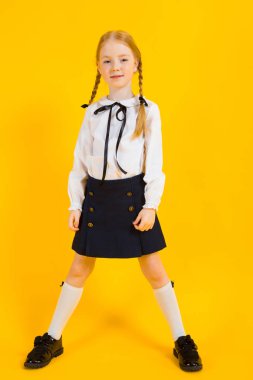 Sarı bir arka plan üzerinde kırmızı pigtails kız. Güzel bir kız ayakta omuzları geniş koymak.