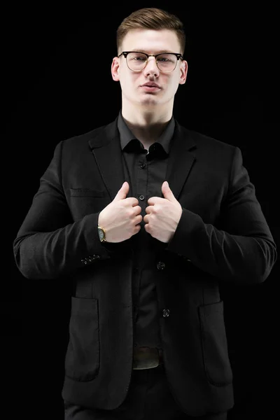 Portrait of confident handsome elegant responsible businessman in glasses holding hands on his suit on black background — Stock Photo, Image