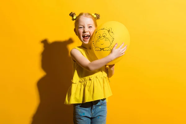 Ragazza con i capelli rossi su sfondo giallo. La ragazza tiene in mano un palloncino giallo e ride . — Foto Stock