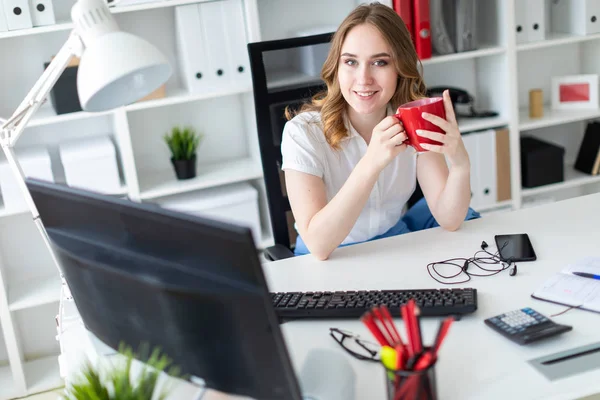 Mooi jong meisje werken met de computer in kantoor. Het meisje heeft een rode kop in haar handen. — Stockfoto