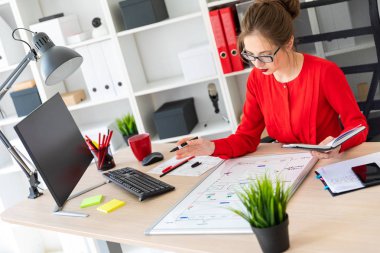 Genç bir kız ofiste bir masada oturuyor, elinde kalem tutan ve bir not defteri ve manyetik bir yönetim kurulu ile çalışır.