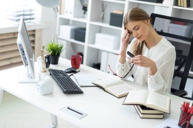 Genç bir kız ofiste bir masada oturuyor, gözlüklerini aldı ve gözlerini ovuşturdu. Önce kız açık bir kitap yatıyor.