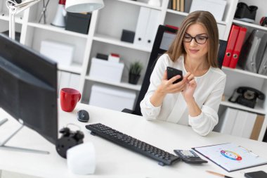 Genç bir kız ofiste masada oturan ve bir telefon tutarak.