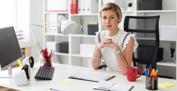 Een jong blond meisje zit achter een computerbureau in het kantoor en een potlood in haar hand houdt. — Stockfoto