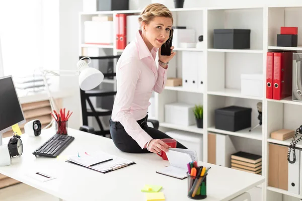 Een jong blond meisje gaat zitten op het Bureau in het kantoor, gesprekken over de telefoon en gespiegeld met de Kladblok. — Stockfoto