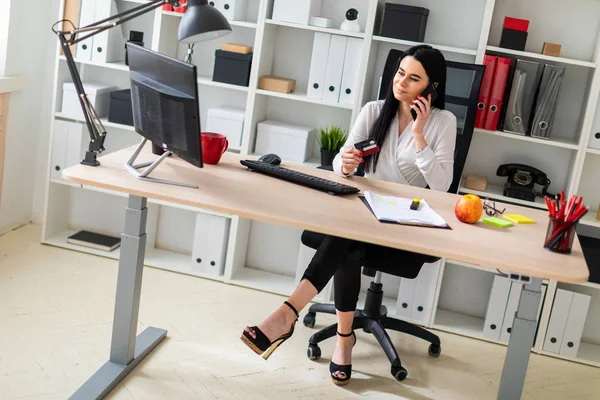 A young girl is sitting at a table, holding a bank card in her hand and talking on the phone.