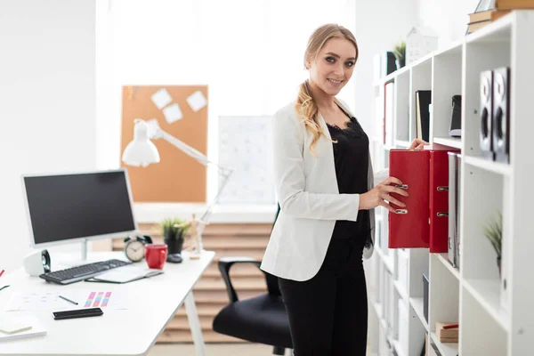 Młoda dziewczyna stoi w pobliżu rack w biurze i wyjmuje folder. — Zdjęcie stockowe