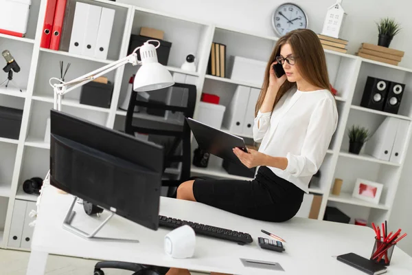 A jovem sentou-se na mesa do escritório, segurando um tablet com lençóis na mão e conversando ao telefone . — Fotografia de Stock