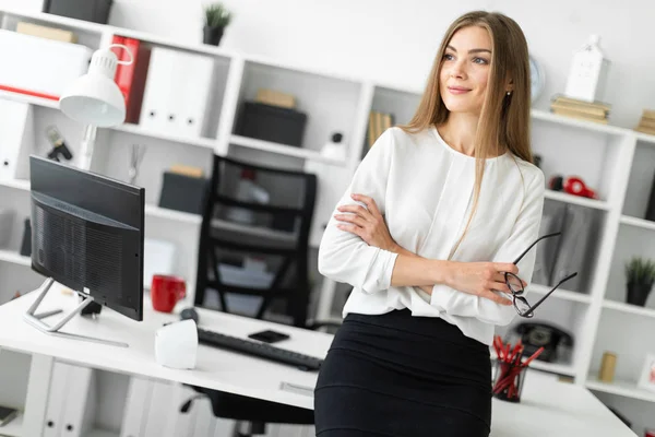 Seorang gadis muda berdiri bersandar di meja di kantor dan memegang kacamata di tangannya . — Stok Foto