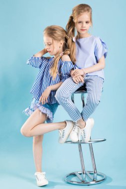 Kızlar ikizler mavi elbise bir barın yakınında poz ışık mavi bir arka plan üzerinde tabure.