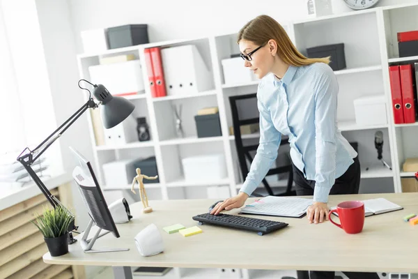 Een jong meisje met een bril staat naast de tafel en drukt op het toetsenbord. — Stockfoto