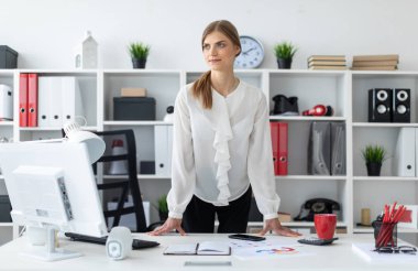 Genç bir kız ofiste bir tabloda hemen yanında duruyor.