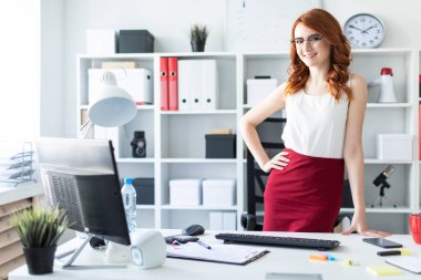 Güzel genç kız office tablo yakın duruyor. Kız bir yandan onun kalça üzerine koydu ve ikinci masanın üzerine eğildi.