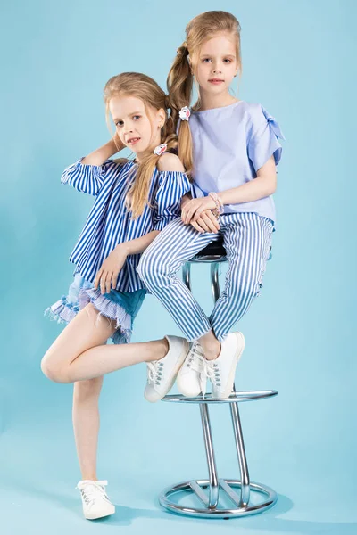 Kızlar ikizler mavi elbise bir barın yakınında poz ışık mavi bir arka plan üzerinde tabure.