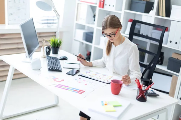 Genç bir kız ofiste bir masada oturmuş, elinde kalem tutan ve belgeye arıyorsunuz.
