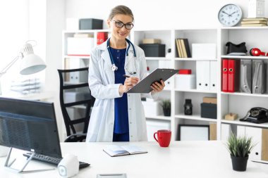 Bir genç kız Beyaz paltolu bir tablo ofisinde yakınındaki duran ve bir tablet ve kalem tutan. Bir stetoskop boynunda asılı.