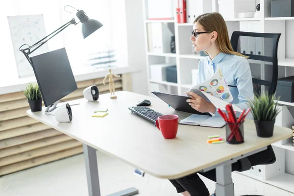 Una joven con gafas se sienta en una mesa en la oficina, sostiene un lápiz en la mano y trabaja con documentos . — Foto de Stock