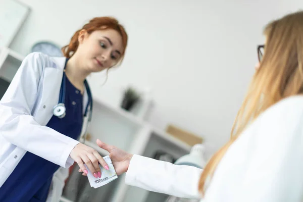 Una bella ragazza in una veste bianca è in piedi vicino a una scrivania del computer in ufficio e comunicare con l'interlocutore. L'interlocutore stringe la mano alle ragazze e le passa i soldi . — Foto Stock