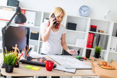 Genç bir kız bir masanın ayakta, telefonda konuşurken ve bir işaretleyici elinde tutan. Masaya manyetik bir pansiyondur. Kızlar kulaklık boynuna asmak.