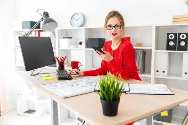 Een jong meisje is permanent aan een tafel in het kantoor, met een zwarte marker en een telefoon in haar hand. Het meisje werkt met een computer, Kladblok en een magneetbord. — Stockfoto