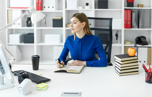 En ung pige sidder ved en computer skrivebord og holder en gul markør i hånden. Før pigen ligger en åben bog . - Stock-foto