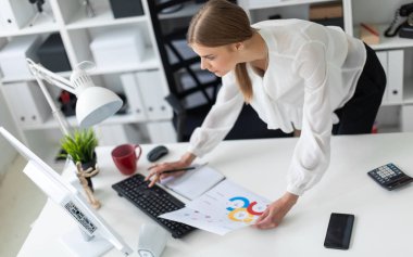 Genç bir kız ofiste bir tabloda yakınındaki bükülmüş duruyor. Kız bir bilgisayar, Not defteri ve belgeler ile çalışır.