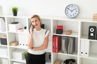 Genç sarışın kız Office belgeleri ile raf yanında duran ve telefonda konuşurken.