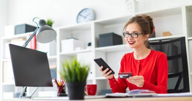 Genç bir kız bir banka kartı ve telefon elinde tutan ofiste, masada oturuyor.