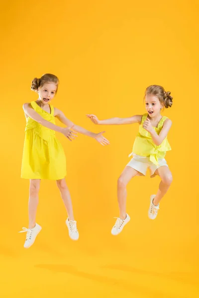 Les filles des jumeaux dansent ensemble sur un fond jaune . — Photo