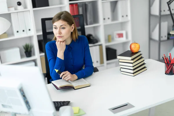 Una joven se sienta en un escritorio de computadora y sostiene un marcador amarillo en su mano. Antes de que la chica mienta un libro abierto . — Foto de Stock