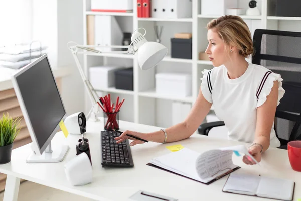 Een jong blond meisje zit achter een computerbureau in het kantoor, houdt een potlood in haar hand en werken met documenten. — Stockfoto