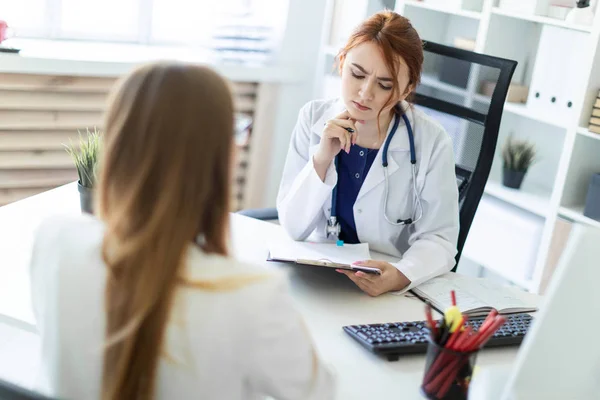 Ein schönes junges Mädchen in weißem Gewand sitzt am Schreibtisch im Büro und kommuniziert mit dem Gesprächspartner. das Mädchen macht Notizen im Blatt. — Stockfoto