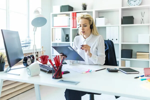 Een jong meisje zit in de koptelefoon met een microfoon op het Bureau in het kantoor en maakt aantekeningen in het document. — Stockfoto