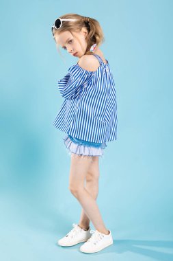 Bir T-shirt ve şort başında gözlüklü bir kız mavi bir arka plan üzerinde duruyor.