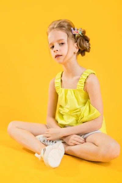 Uma adolescente está sentada em um fundo amarelo . — Fotografia de Stock