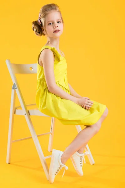 Ein Mädchen sitzt auf einem weißen Stuhl auf gelbem Hintergrund. — Stockfoto