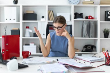 Genç bir kız ofiste masasında oturmuş, elinde kalem tutan ve belgeleriyle çalışma.