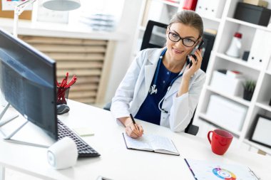 Beyaz bir elbise içinde genç bir kız ofiste masada oturan, telefonda konuşurken ve onun elinde kalem tutan. Bir stetoskop boynunda asılı.